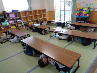 地震が起きて机の下に避難しているところ