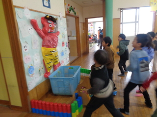 ホールの鬼へ”オニはそと”と作った豆をまく子どもたち